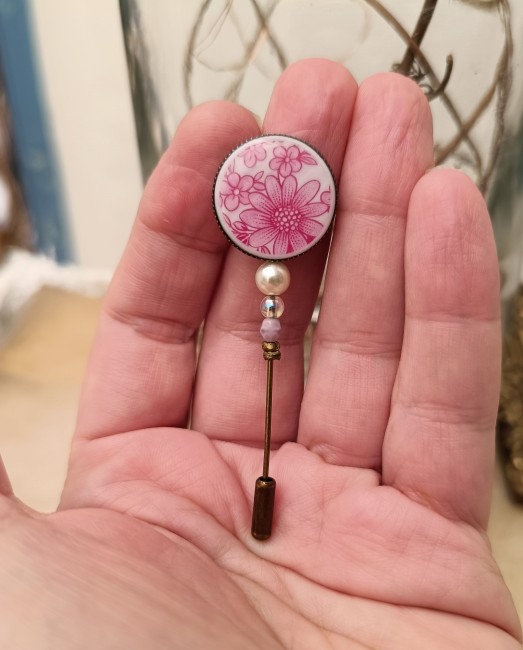 Fibule fleurs roses présentée en main pour apprécier ses dimensions et ses détails.