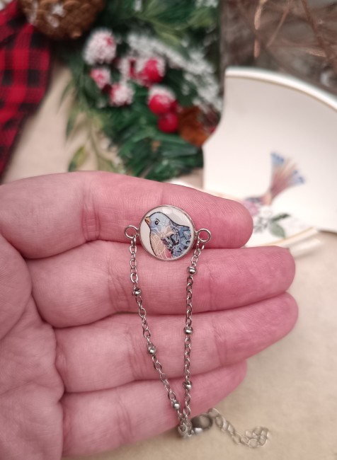 Bracelet À la Volette en porcelaine transformée tenu dans la main pour montrer la finesse du motif d’oiseau.