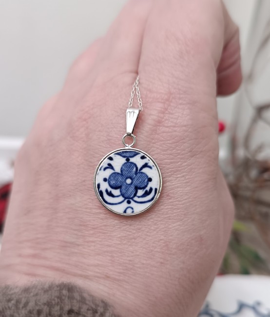 Photo du collier en faïence de Moustiers tenu dans les mains. Pièce unique façonnée à partir d’une assiette fendue. Bijou artisanal durable et poétique.