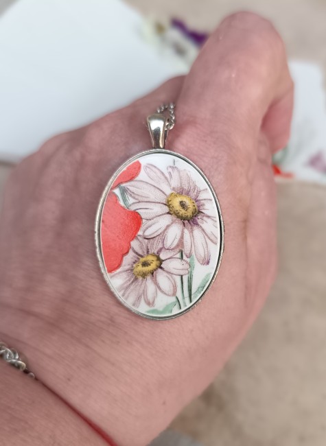 Gros plan sur le pendentif pour apprécier la finesse du motif floral et les détails de la faïence ancienne.