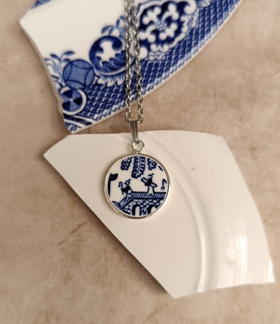 Collier en porcelaine anglaise Blue Willow recyclée sur fond blanc, pendentif plaqué argent fabriqué artisanalement en France et chaîne en acier inoxydable.