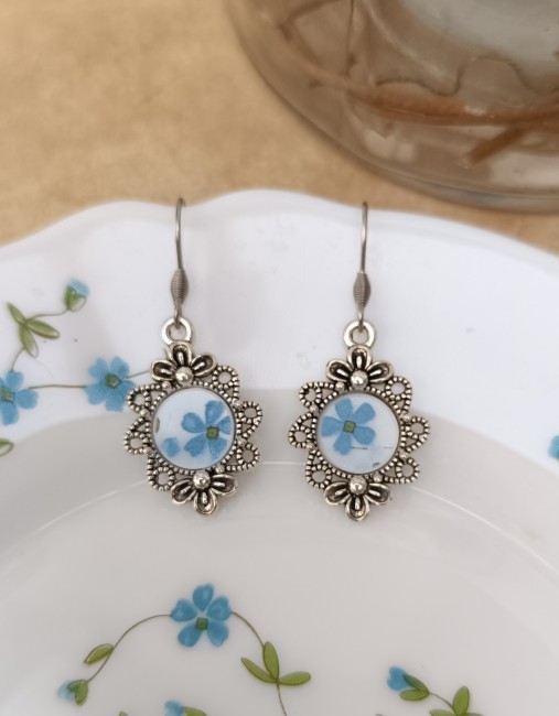 Boucles d'oreilles Myosotis en Arcopal recyclé sur fond blanc, montées sur des apprêts en acier inoxydable.