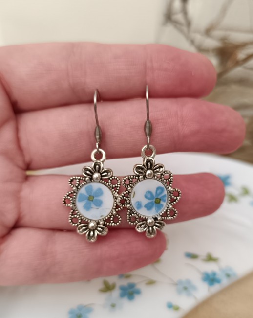Boucles d'oreilles Myosotis présentées en main pour apprécier les dimensions réelles et les détails du motif floral.