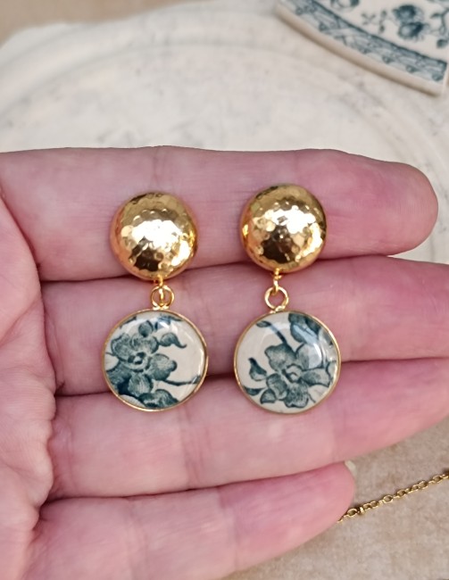 Boucles d'oreilles présentées en main pour apprécier les dimensions et les détails du décor d'origine.