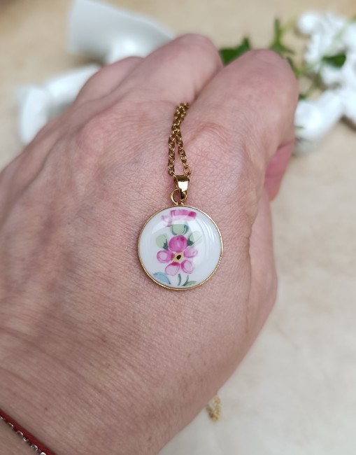 collier-poesie-porcelaine-baviere-18mm-main Collier Poésie présenté en main pour visualiser les proportions de son pendentif floral de 18 mm en porcelaine ancienne.