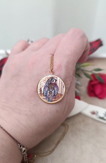 Le collier À la Volette présenté en main pour révéler la finesse du pendentif en porcelaine ancienne transformée.