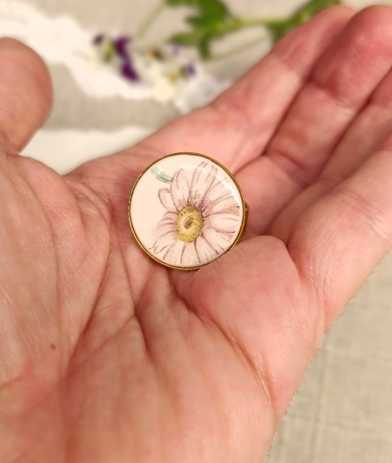 Grande bague présentée en main pour apprécier les dimensions du cabochon rond de 22 mm et les détails du motif marguerite.