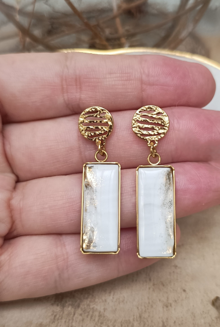 Boucles d'oreilles Célestes présentées en main pour apprécier leur format rectangulaire de 10 × 30 mm et la finesse du filet doré.