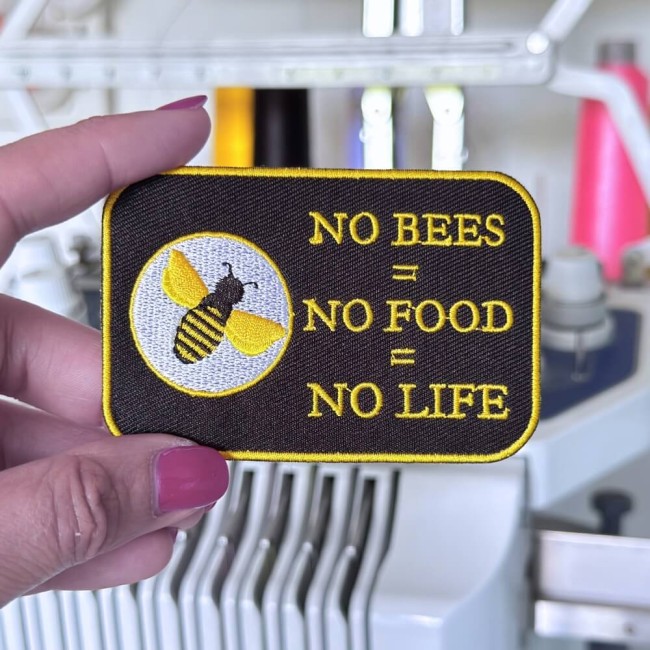 Patch abeille brodé tenu dans ma main devant ma machine à broder