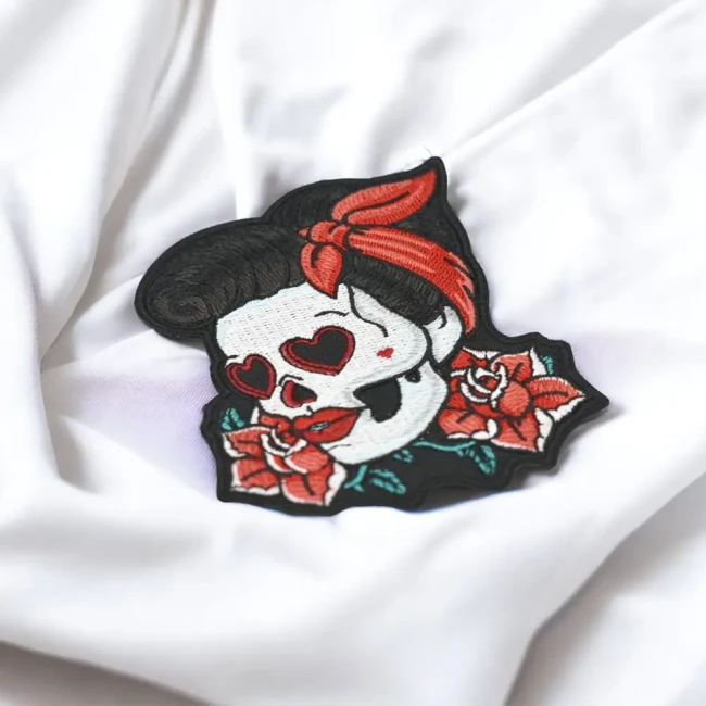 Patch tête de mort pin-up brune présenté sur un tissu blanc Patch brodé pin-up blonde sugar skull entourée de roses
