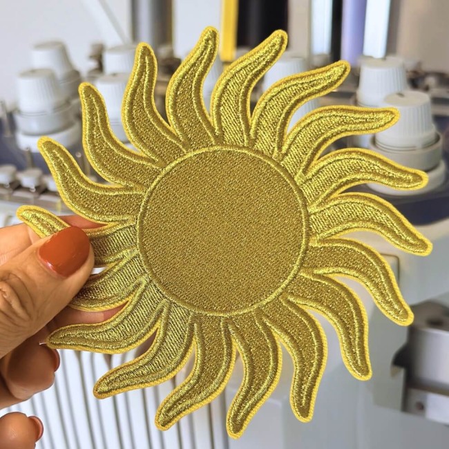 Patch soleil doré brodé présenté en main pour montrer sa taille