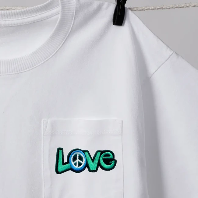 Patch LOVE peace brodé vert et bleu – customisation textile Patch brodé thermocollant LOVE vert avec symbole peace bleu, posé sur tissu blanc