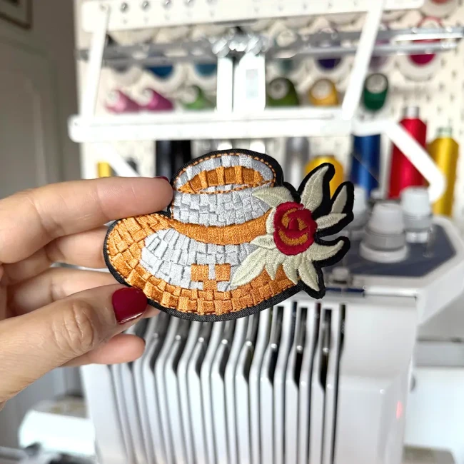 Patch chapeau de paille fleuri tenu devant une machine à broder