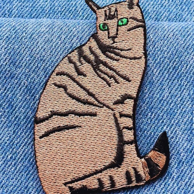 Patch chat brodé marron rayé posé sur tissu denim, gros plan motif et couleurs
