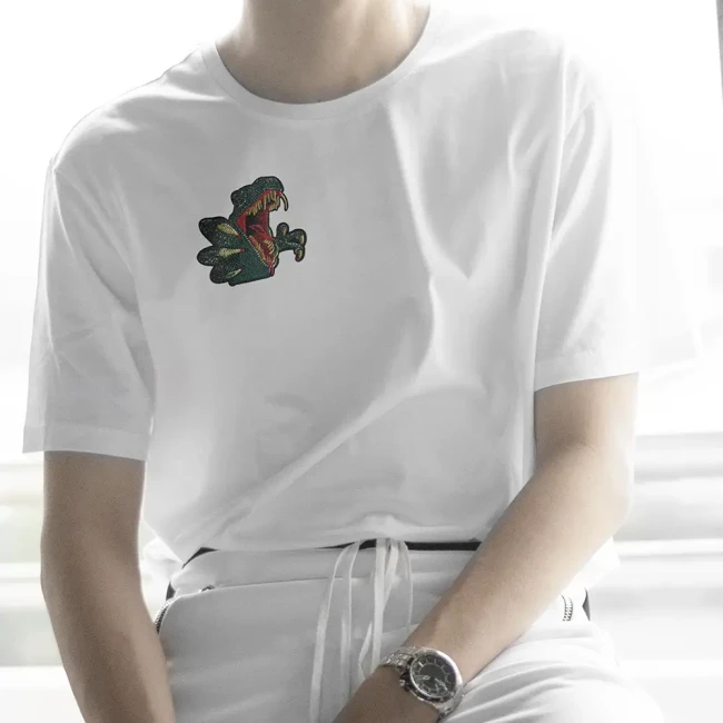 Patch dinosaure brodé porté sur un T-shirt blanc