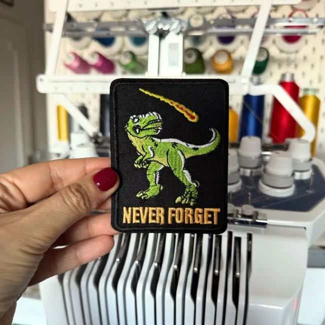 Patch T-Rex Never Forget tenu devant une machine à broder