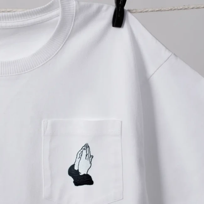 Écusson brodé mains en prière sur tee-shirt blanc Patch mains en prière posé sur la poche d’un tee-shirt blanc