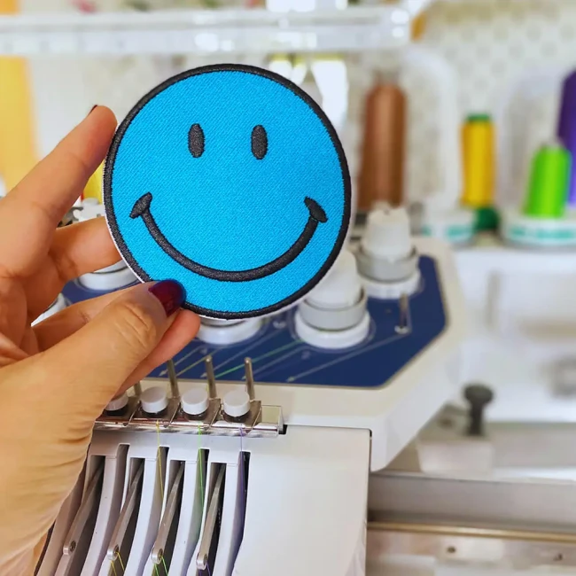 Écusson smiley bleu pour customiser vote vêtement préféré et brodé dans mon atelier Patch smiley bleu turquoise tenue dans ma main devant ma machine à broder