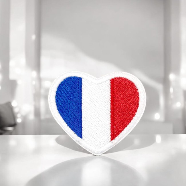 Patch en forme de cœur tricolore debout sur fond clair, avec un relief brodé qui reflète la qualité artisanale du produit