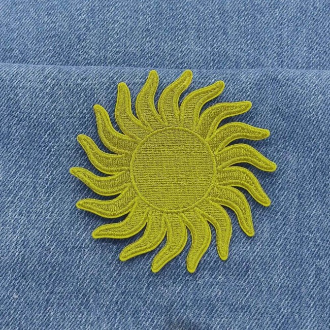 Écusson soleil brodé de fil or métallique posé sur un jean bleu Patch soleil doré thermocollant posé sur un jean