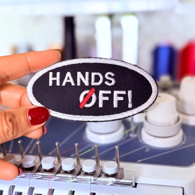 Photo de l'écusson thermocollant prise devant ma machine à broder Patch brodé oval blanc sur fond noir. Photo atelier