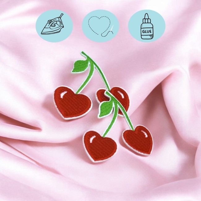 atchs cerises cœur brodés – Détail et texture Gros plan sur plusieurs patchs cerises cœur brodés, posés sur un tissu rose satiné.