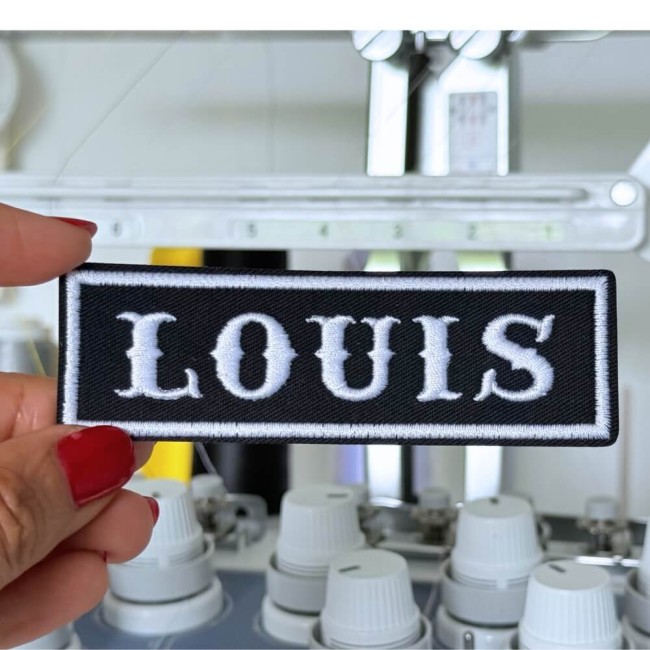 Détail atelier patch prénom Louis Patch prénom Louis brodé noir et blanc devant machine à broder