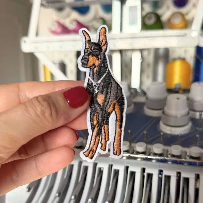 Patch Dobermann brodé tenu devant une machine à broder