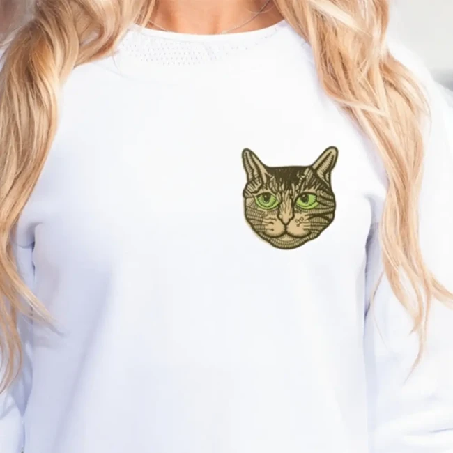 Patch chat tigré beige aux yeux verts posé sur un sweat blanc