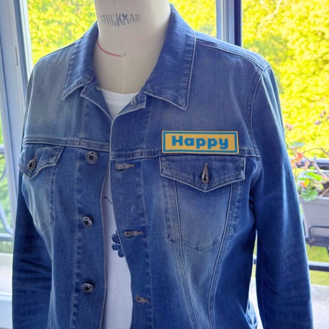 Patch mot au choix, ici le mot Happy sur veste en jean Gros plan sur le patch mot personnalisé Happy brodé sur veste en jean
