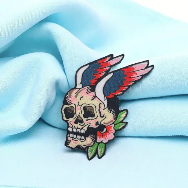 Écusson tête de mort ailée rouge et bleue sur tissu bleu clair Crâne ailé avec fleur et ailes brodées