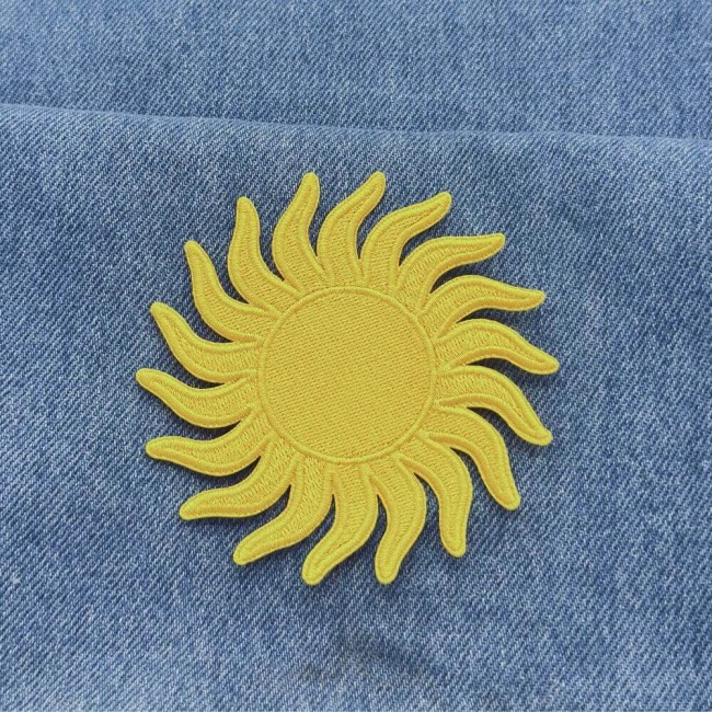 Écusson soleil jaune posé sur un jean bleu Patch soleil jaune thermocollant posé sur un jean