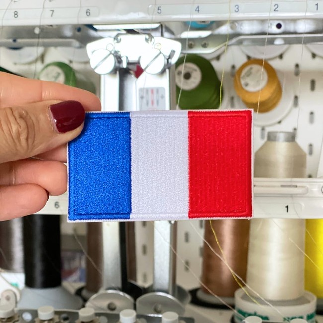Zoom sur patch rectangle bleu blanc rouge tenu devant une machine à broder dans un atelier