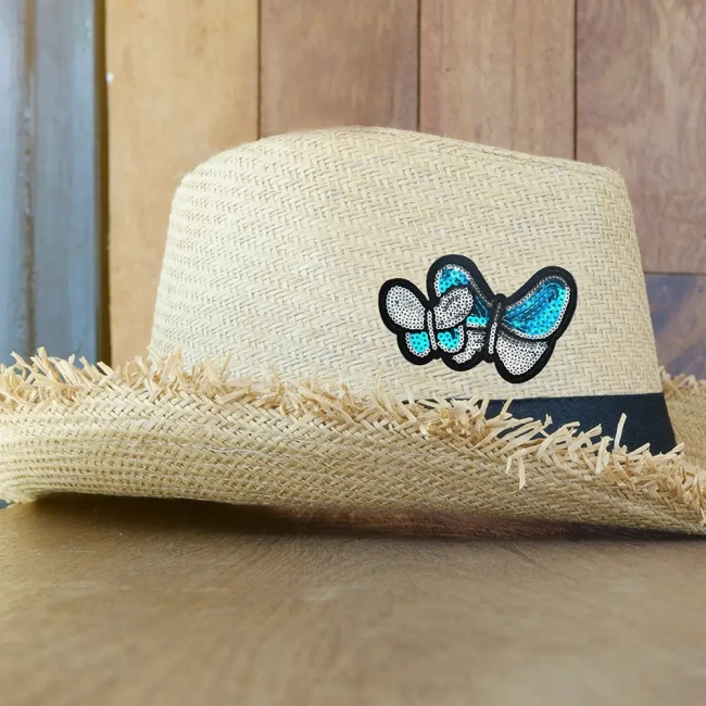 Écusson papillons bleu et argent sur chapeau atch papillons à sequins posé sur un chapeau de paille