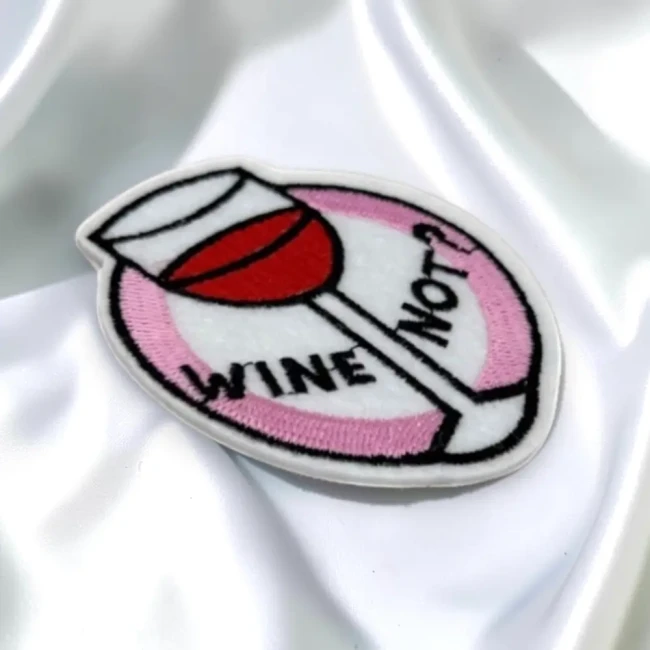 Détail du patch brodé Wine Not? sur tissu blanc