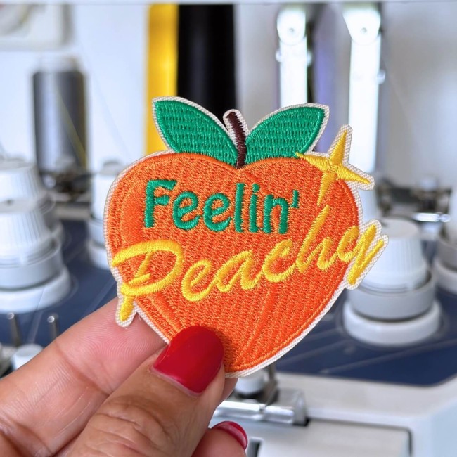 Patch brodé pêche avec le texte feelin' peachy tenu dans ma main devant la machine à broder
