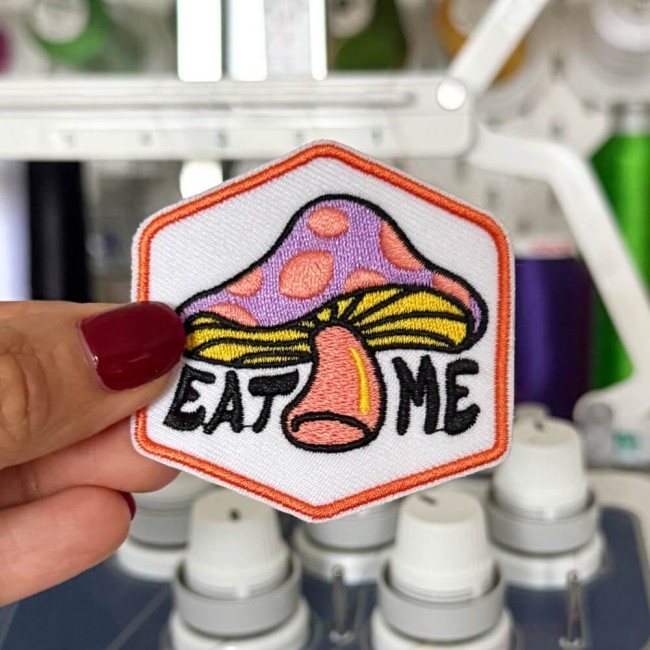 patch brodé coloré fun et rétro Ecusson psychédélique EAT ME avec bordure orange tenue dans ma main devant ma machine à broder