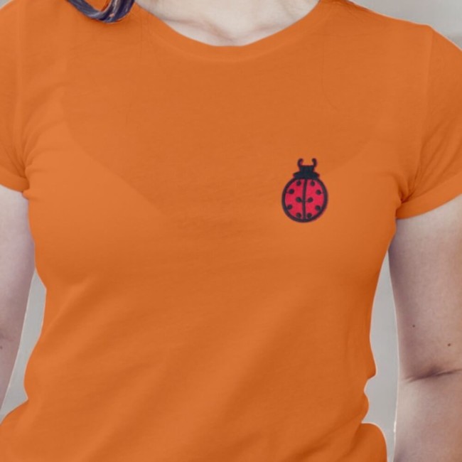 Tee-shirt orange portée par une femme avec l'écusson coccinelle thermocollé sur la poitrine
