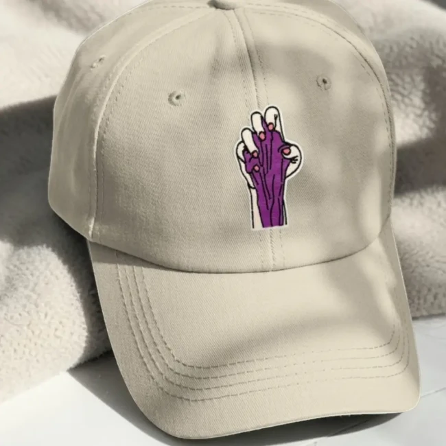 Patch brodé main anatomique sur casquette beige Patch main anatomique violette posé sur une casquette beige