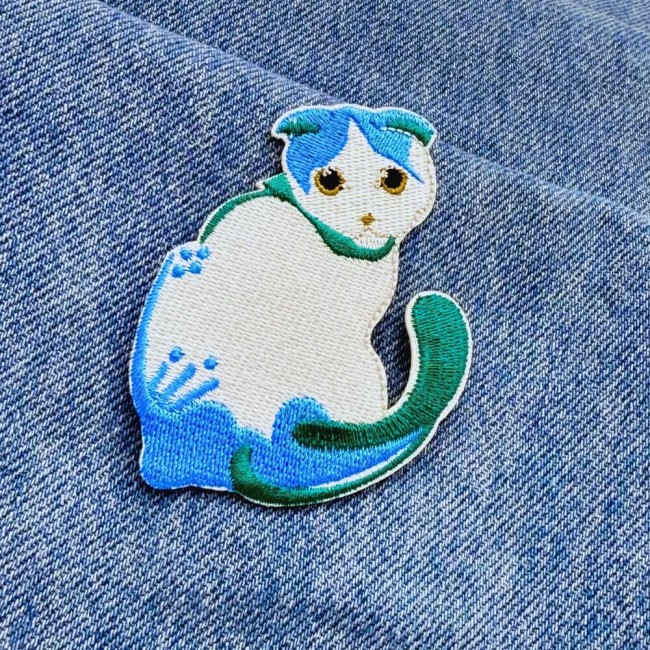 Patch chat brodé bleu posé sur tissu denim, zoom motif et couleurs