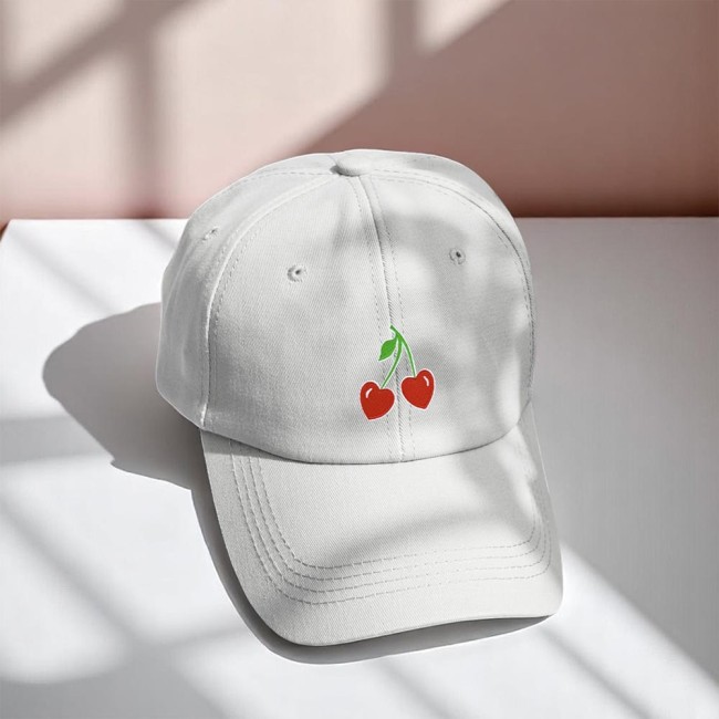 Écusson cerises cœur – Customisation casquette Patch cerises cœur brodé sur une casquette blanche, lumière naturelle et ambiance pastel.