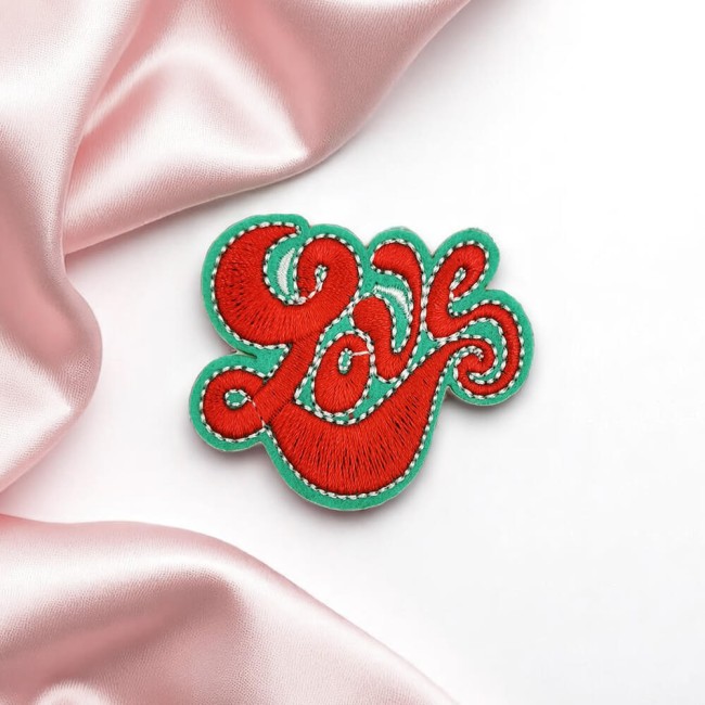 Écusson LOVE rouge et vert posé sur tissu rose satiné