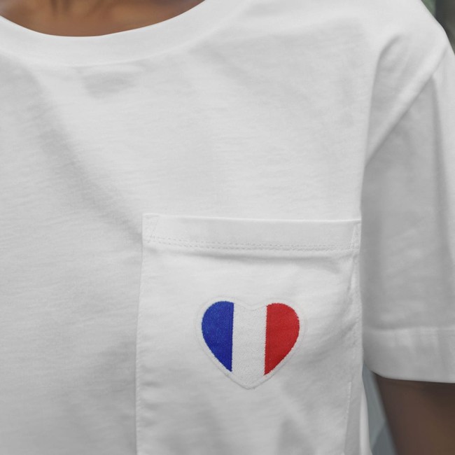 Détail d’un t-shirt orné du patch cœur bleu blanc rouge appliqué sur une poche poitrine, pour un rendu chic et patriotique.