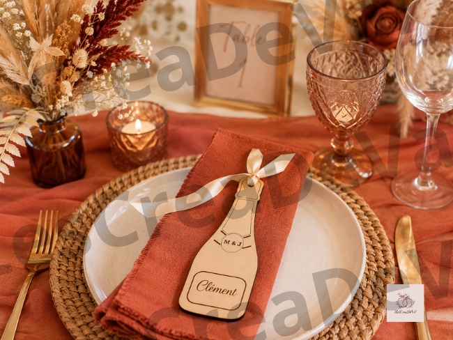 Porte-nom bouteille de champagne personnalisé ambiance terracotta Porte-nom mariage en bois personnalisé en forme de bouteille de champagne présenté sur une table de mariage terracotta avec ruban satin